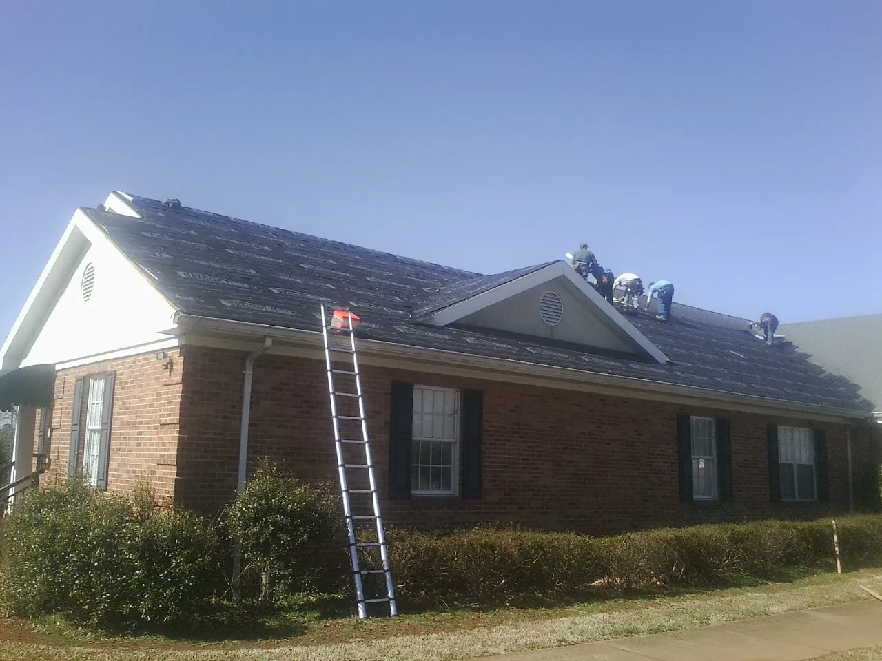 Crew tearing shingles off a brick ranch roof with a ladder set — Emergency Roof Repair work by our crew in Green Pond